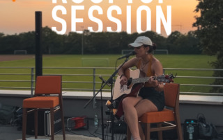 Rooftop Session im Juni auf der Dachterrasse. Eine Sängerin mit Gitarre trägt vor